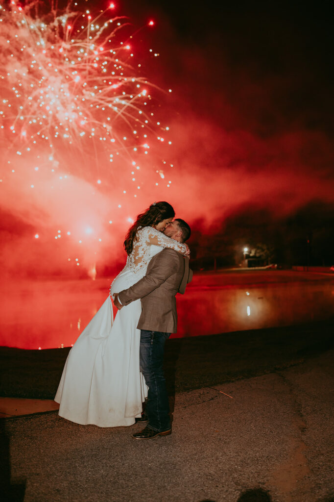 groom kissing the bride with fireworks in the background 
