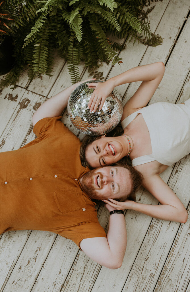 Couple laying on the ground smiling with a disco ball