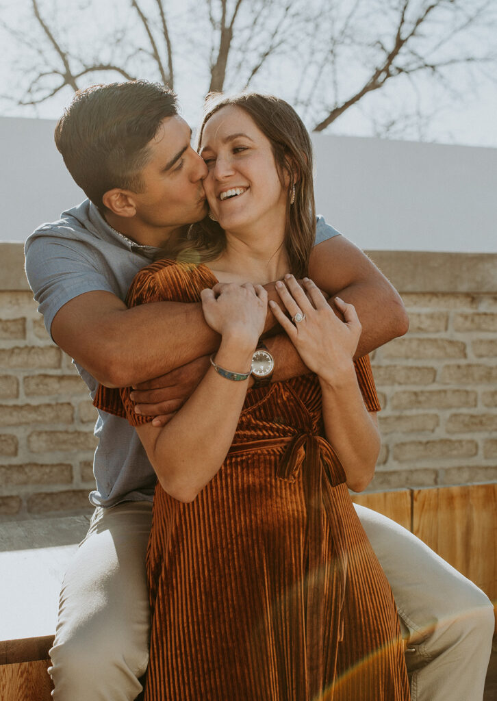 stunning fiance kissing his fiance on the cheek during their adventurous engagement photoshoot 