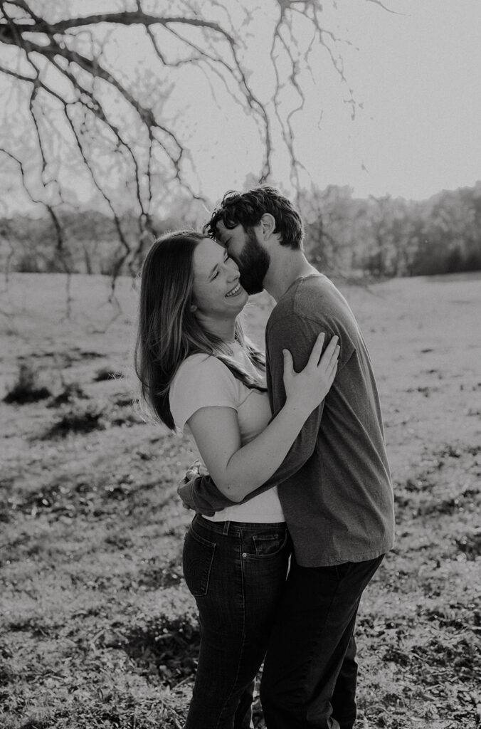 b&w photo of the newly engaged couple kissing on the cheek